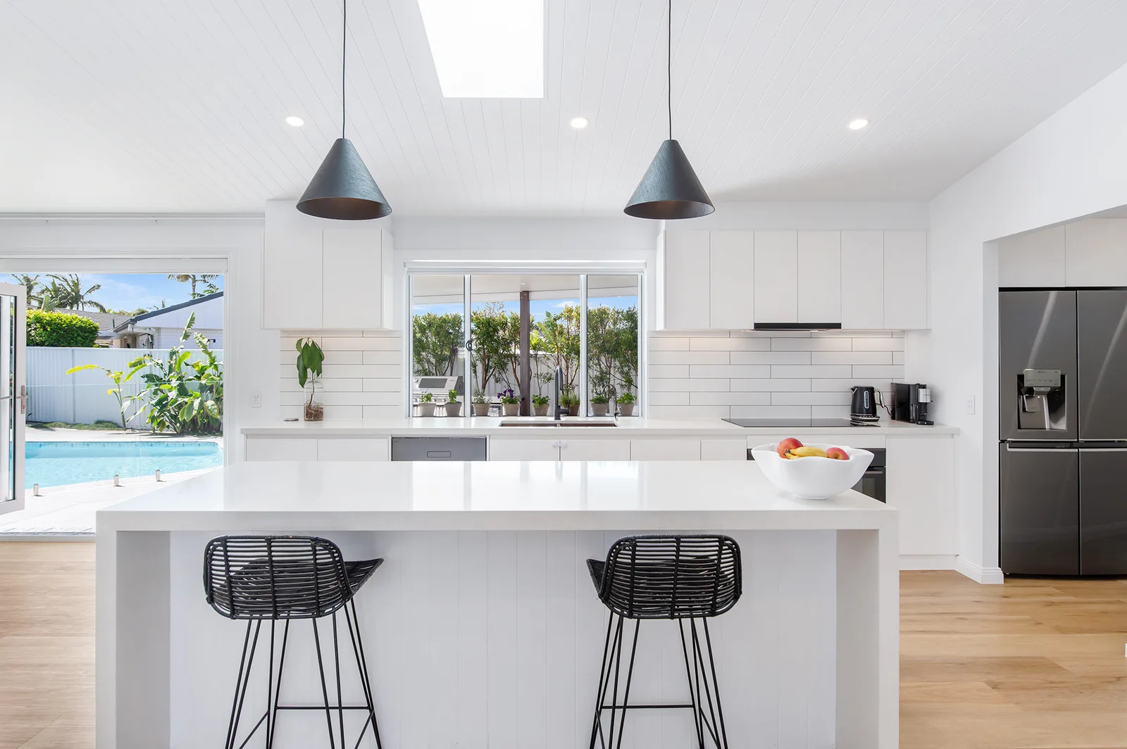 Light-filled kitchen with a large island, skylight and doors opening towards the private pool