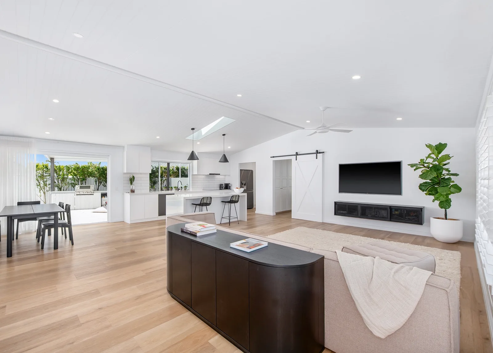 Open living and dining room with soaring white timber ceilings, skylights and pale oak floors
